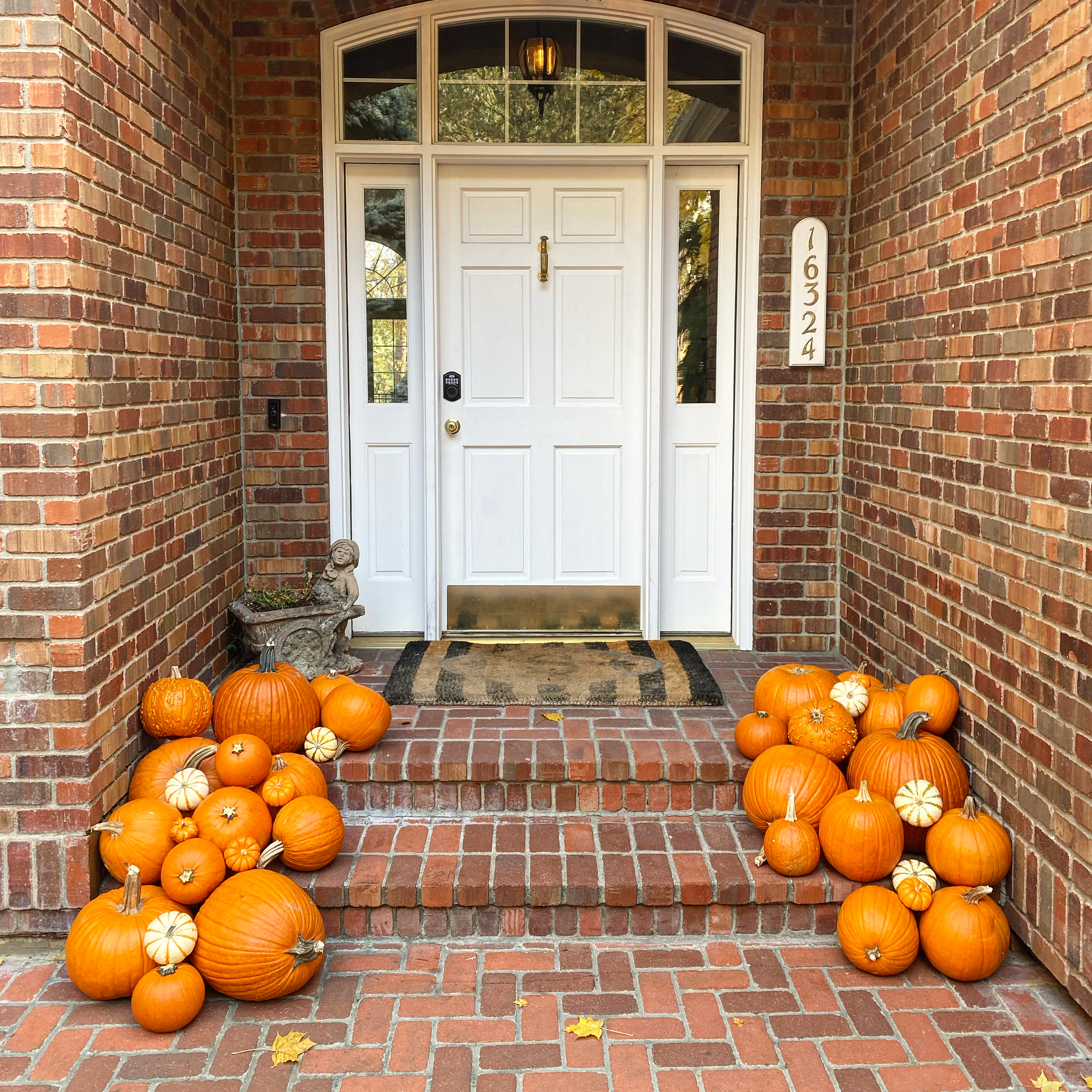 Brick front porch styled with layered orange and white pumpkins