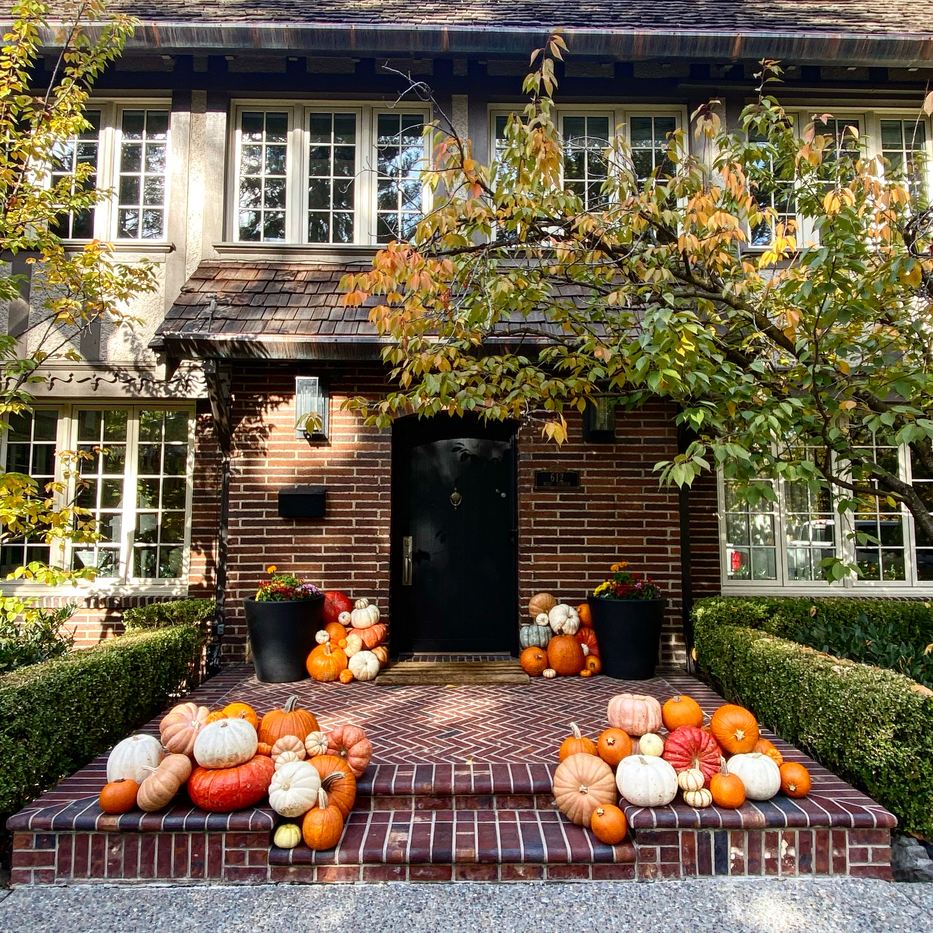 Brick front porch decorated with layered pumpkins and autumn planters